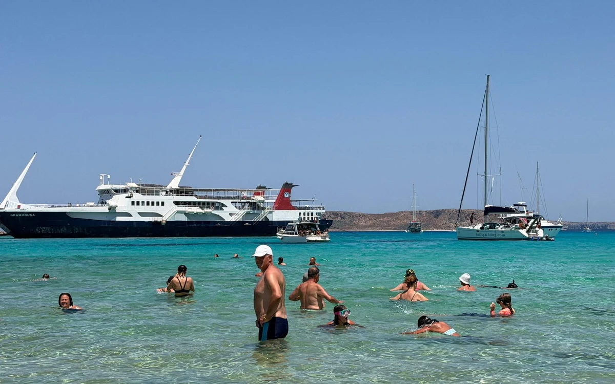 A large white ferry offshore with swimmers standing in the shallow water