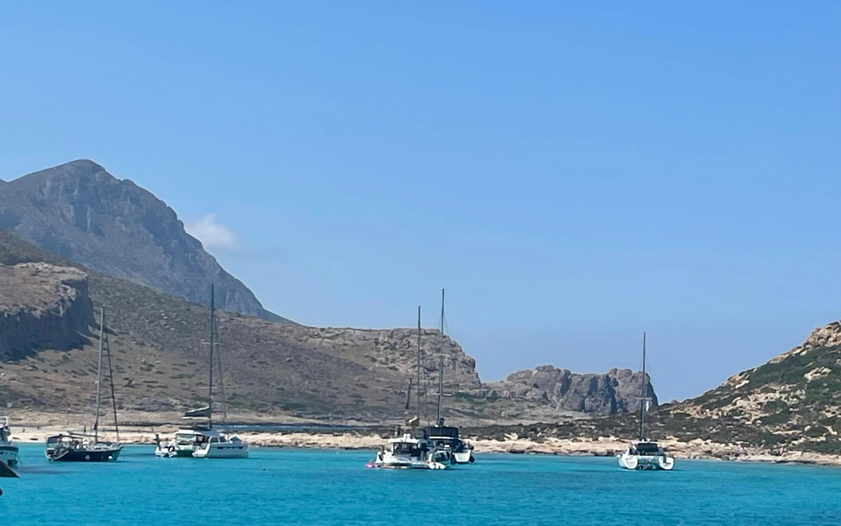 Sailing boats moored in clear blue water below rocky hills