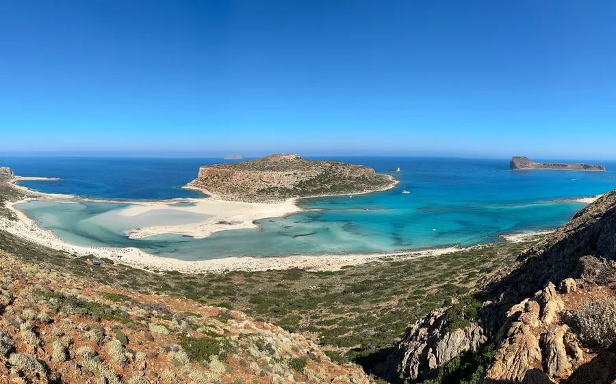 The lagoon and its rocky islet from a hillside above pale shallows