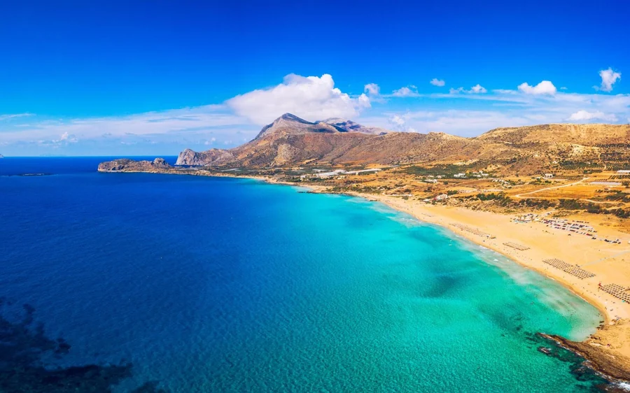 A long sandy beach and turquoise sea seen from a hillside