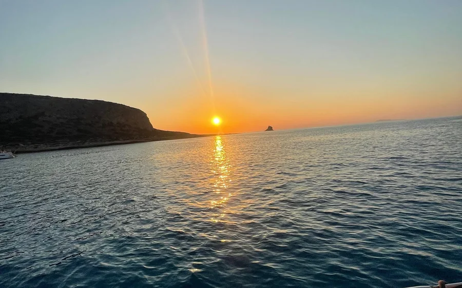 The sun low over the sea beside a dark headland