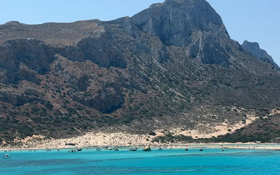 A steep rocky mountainside above a strip of sand and turquoise water
