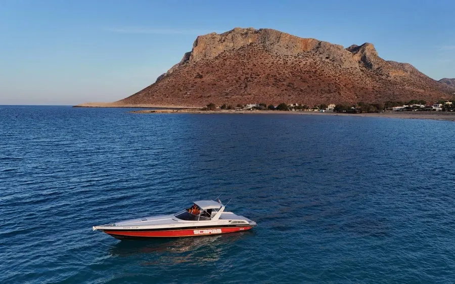 A red and white powerboat on deep blue water below a rocky island