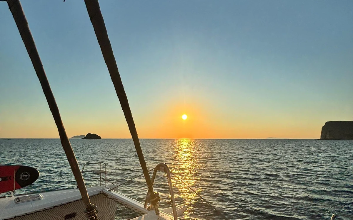 The sun low over the sea, seen between the rigging of a sailing catamaran